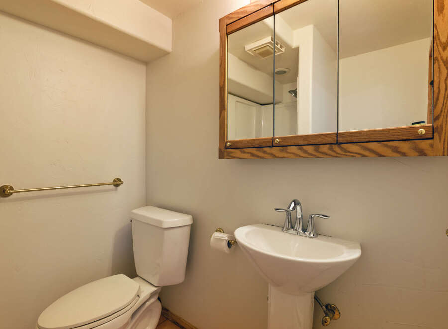 This charming bathroom boasts a classic pedestal sink and toilet, complemented by a wood-framed medicine cabinet.