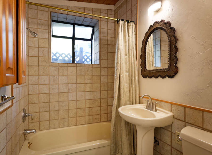 This charming bathroom boasts a vintage-inspired pedestal sink and ornate mirror, complementing the classic beige tile and wooden accents.