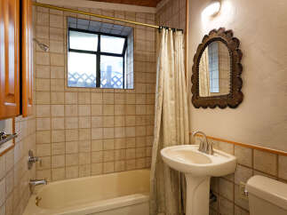 This charming bathroom boasts a vintage-inspired pedestal sink and ornate mirror, complementing the classic beige tile and wooden accents.
