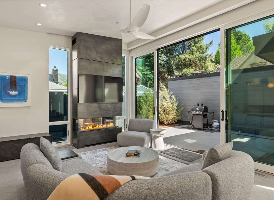 Modern living room with a stunning fireplace and large sliding glass doors leading to a patio with a grill.