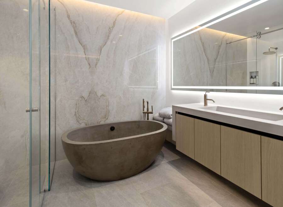 Luxurious bathroom boasts a freestanding concrete tub and a double vanity with sleek wooden cabinets.
