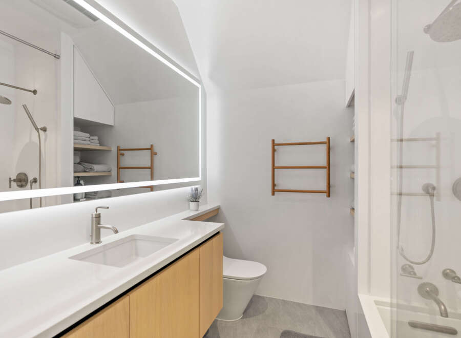This stunning bathroom boasts a modern design with sleek white finishes and light oak cabinetry.