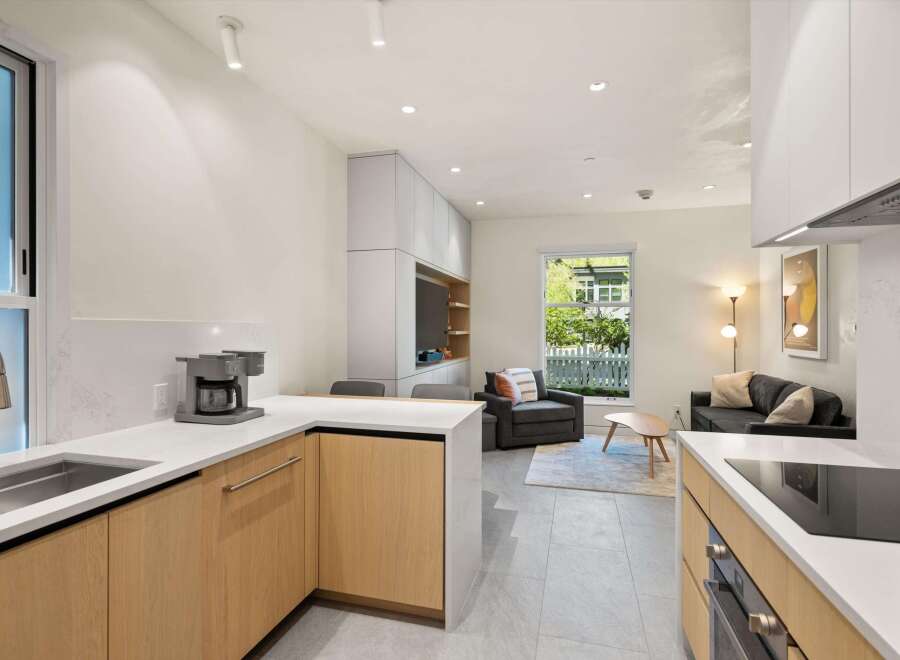 Modern kitchen with light wood cabinets and quartz countertops, open to a living area with comfortable seating and large windows.
