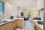 Modern kitchen with light wood cabinets and quartz countertops, open to a living area with comfortable seating and large windows.