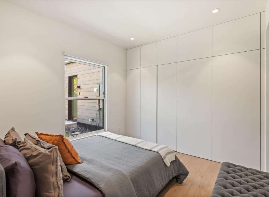 This bedroom boasts a serene atmosphere with its minimalist design and large window offering ample natural light.