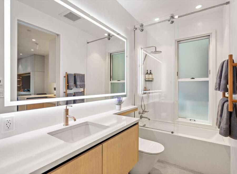 This stunning bathroom boasts a modern design with a sleek, illuminated mirror and a spacious walk-in shower.