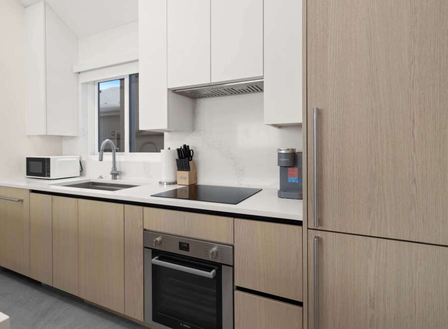 Modern kitchen with light wood cabinets, stainless steel appliances, and quartz countertops.