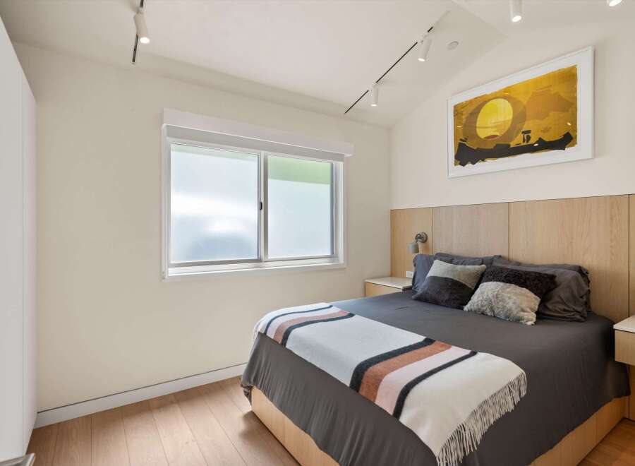This stunning bedroom boasts a cozy and modern design, featuring a plush gray bed with a striped throw blanket and a light oak wood headboard.