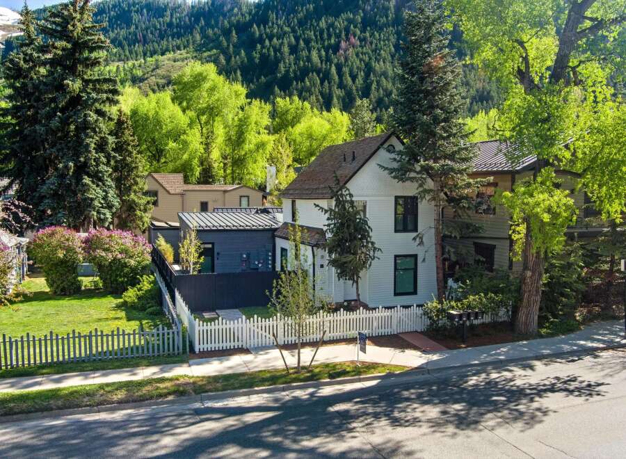 Charming white house nestled in a mountain setting with a modern, dark gray addition.