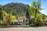 Charming white house nestled in a mountain setting, featuring a picket fence and mature trees.