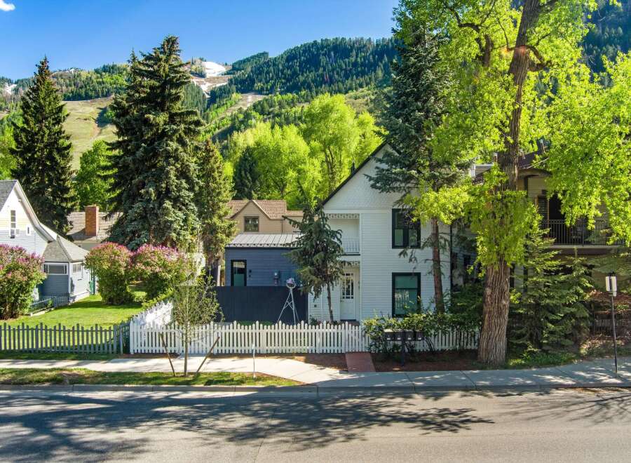 Charming white house nestled in a mountain town setting, featuring a picket fence and mature landscaping.