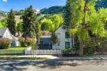 Charming white house nestled in a mountain town setting, featuring a picket fence and mature landscaping.