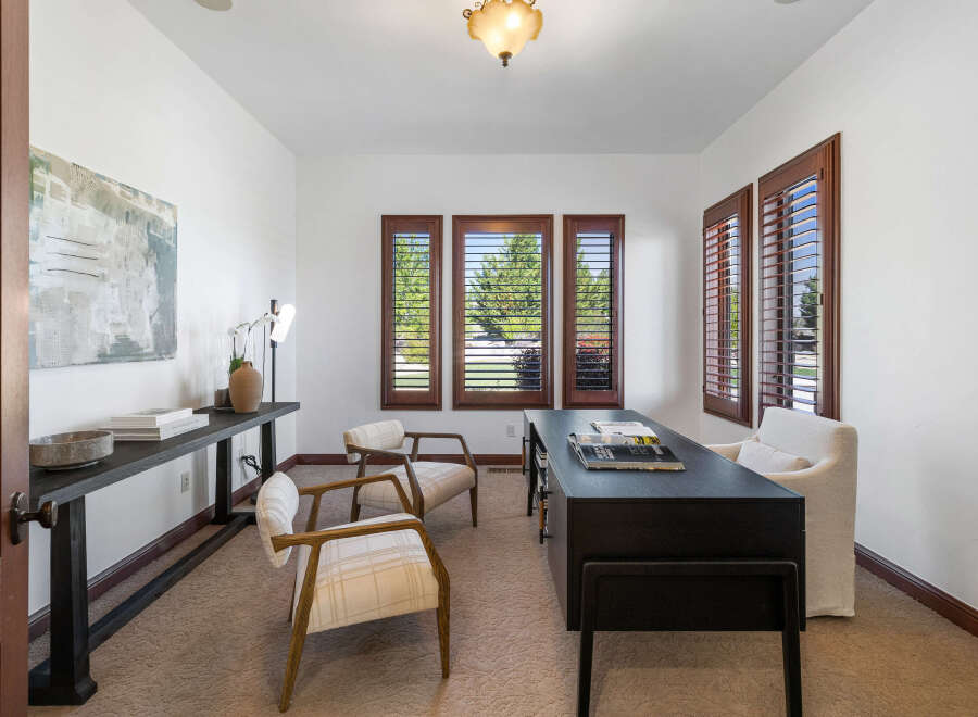 This home office boasts a serene atmosphere with natural light streaming through large windows adorned with plantation shutters.