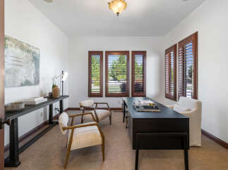 This home office boasts a serene atmosphere with natural light streaming through large windows adorned with plantation shutters.