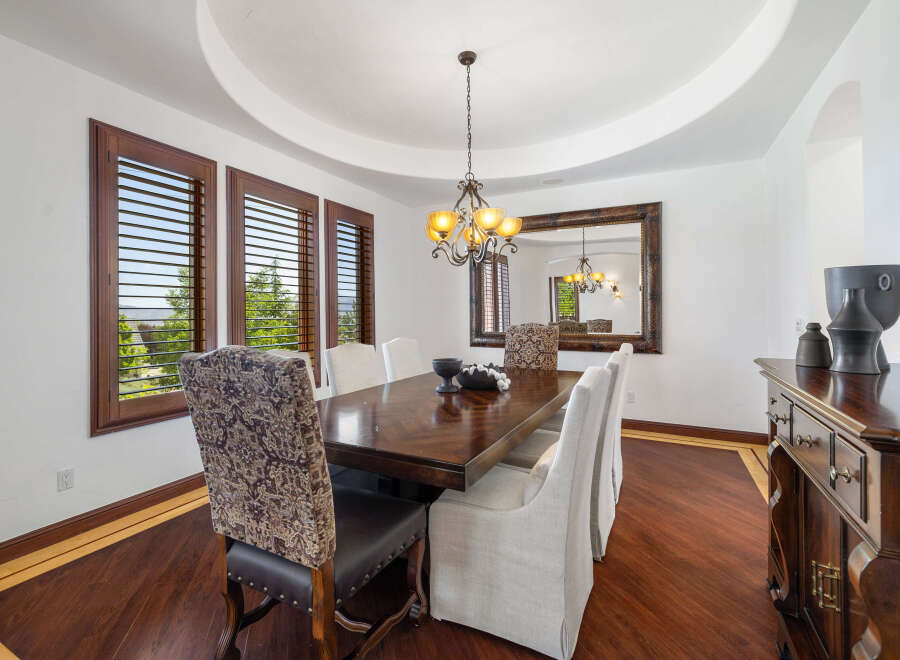 This elegant dining room boasts a stunning hardwood floor, complemented by rich wood furniture and large windows with plantation shutters.