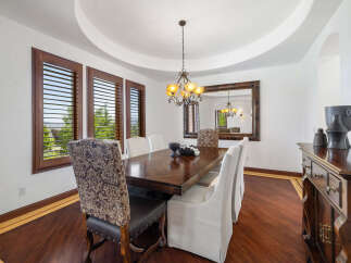 This elegant dining room boasts a stunning hardwood floor, complemented by rich wood furniture and large windows with plantation shutters.