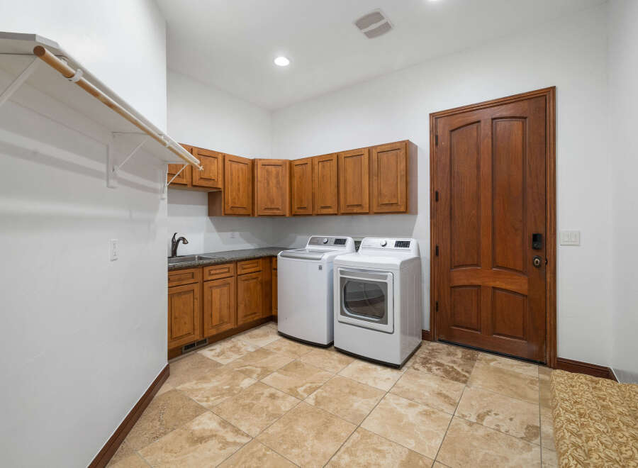 This stunning laundry room boasts ample storage with custom wood cabinets and a convenient built-in hanging rod.