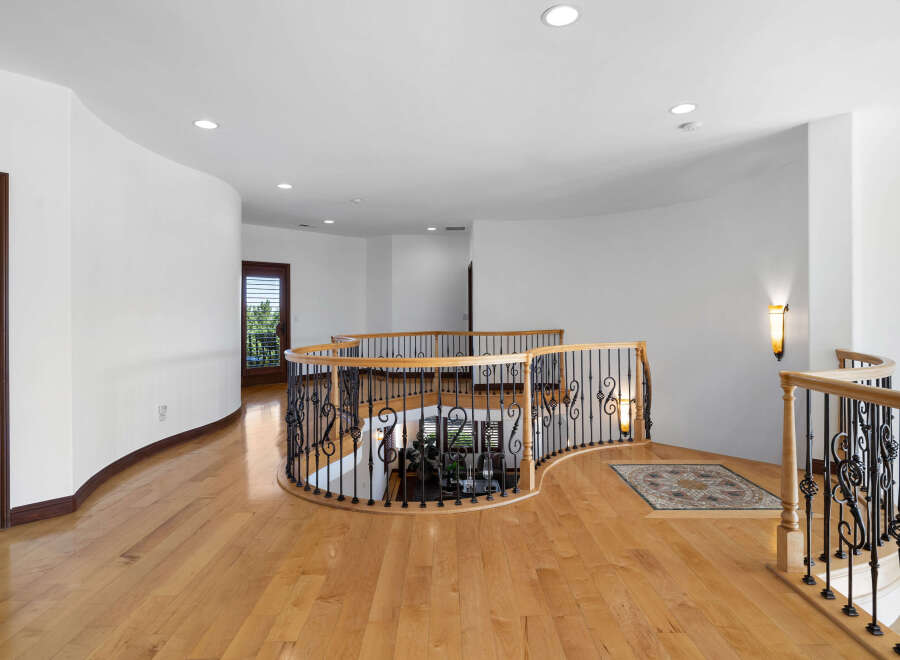 This stunning property boasts a grand curved staircase with intricate wrought iron railings and rich hardwood floors.
