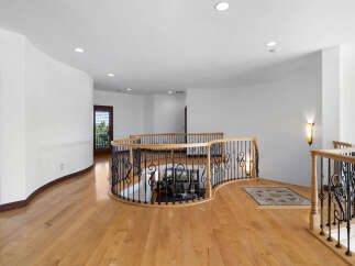 This stunning property boasts a grand curved staircase with intricate wrought iron railings and rich hardwood floors.