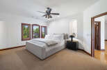This bedroom boasts a serene atmosphere with plush carpeting, large windows offering abundant natural light, and a ceiling fan for comfort.