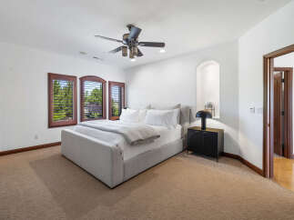 This bedroom boasts a serene atmosphere with plush carpeting, large windows offering abundant natural light, and a ceiling fan for comfort.