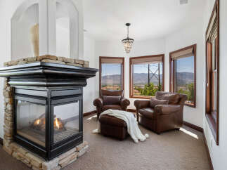 Cozy up by the fireplace in this stunning room, featuring a stone fireplace and large windows offering breathtaking views.
