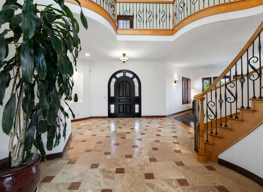 This stunning home boasts a grand foyer with a beautiful travertine tile floor, a sweeping staircase with wrought iron railings, and a dramatic arched entry door.