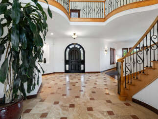 This stunning home boasts a grand foyer with a beautiful travertine tile floor, a sweeping staircase with wrought iron railings, and a dramatic arched entry door.
