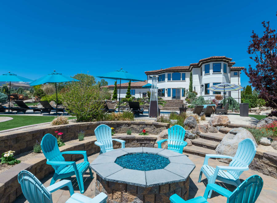 This stunning property boasts a luxurious outdoor space, complete with a fire pit, comfortable seating, and multiple umbrellas for shade.