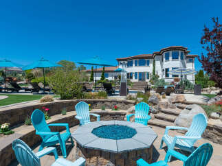 This stunning property boasts a luxurious outdoor space, complete with a fire pit, comfortable seating, and multiple umbrellas for shade.