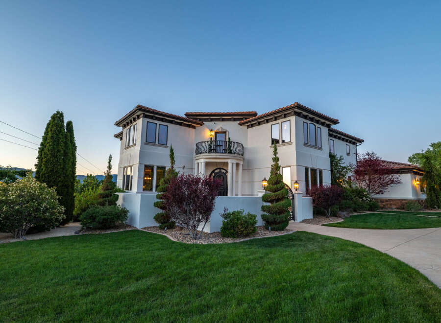 This stunning Mediterranean-style home boasts a large, beautifully landscaped yard with lush green grass and mature trees.