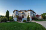 This stunning Mediterranean-style home boasts a large, beautifully landscaped yard with lush green grass and mature trees.