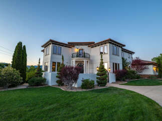 This stunning Mediterranean-style home boasts a large, beautifully landscaped yard with lush green grass and mature trees.