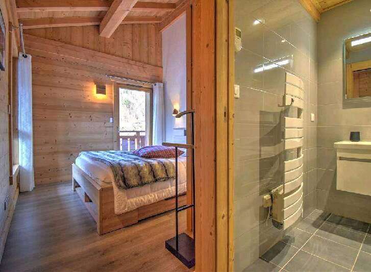 Cozy chalet bedroom with wooden walls and a comfortable bed, featuring an ensuite bathroom with modern fixtures and a heated towel rack.
