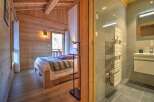 Cozy chalet bedroom with wooden walls and a comfortable bed, featuring an ensuite bathroom with modern fixtures and a heated towel rack.