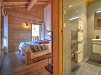 Cozy chalet bedroom with wooden walls and a comfortable bed, featuring an ensuite bathroom with modern fixtures and a heated towel rack.