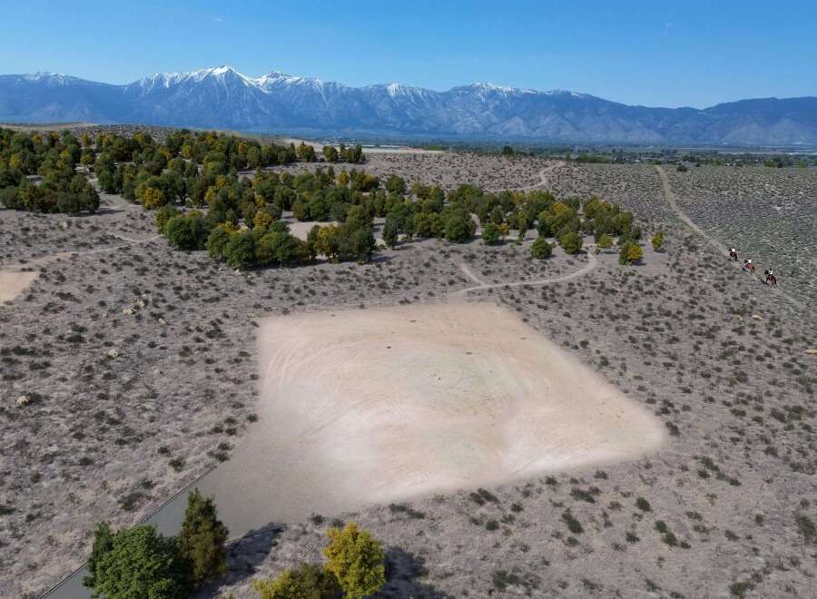 This property boasts a unique, flat, sandy area perfect for various recreational activities, surrounded by a landscape of shrubs and trees.