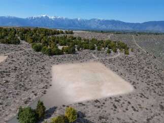 This property boasts a unique, flat, sandy area perfect for various recreational activities, surrounded by a landscape of shrubs and trees.