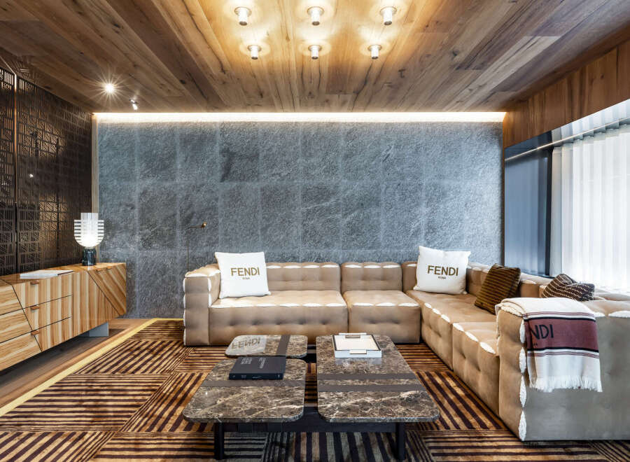 Luxury living room with Fendi decor, featuring a large sectional sofa, marble coffee tables, and a wood-paneled ceiling.
