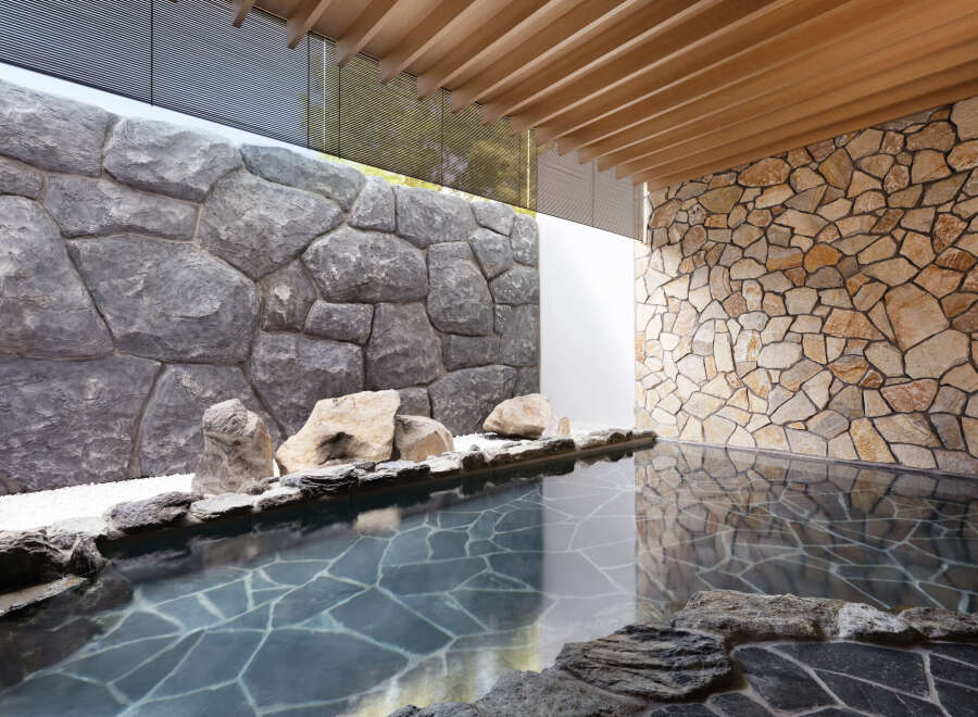 Indulge in tranquility at this luxurious onsen, featuring a serene outdoor bath nestled between stunning stone walls.