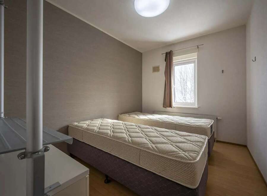 Cozy twin bedroom with neutral wall tones and natural light from a window.