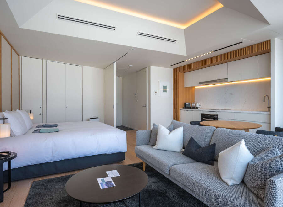 Modern studio apartment featuring a comfortable queen-size bed, a stylish grey sofa, and a fully equipped kitchenette.