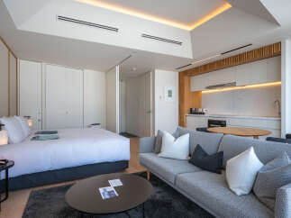 Modern studio apartment featuring a comfortable queen-size bed, a stylish grey sofa, and a fully equipped kitchenette.