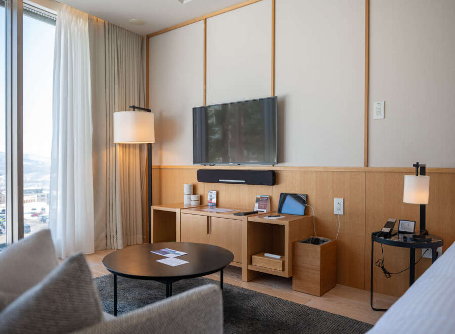 Relax in style in this modern hotel room, featuring floor-to-ceiling windows with mountain views, a comfortable seating area, and a sleek entertainment center.
