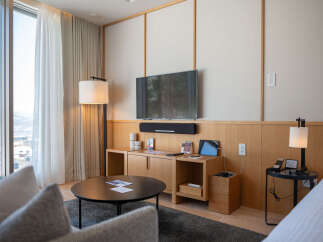 Relax in style in this modern hotel room, featuring floor-to-ceiling windows with mountain views, a comfortable seating area, and a sleek entertainment center.