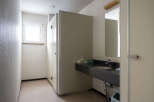 This clean and simple restroom features a single sink vanity with a dark countertop and a light beige wall.