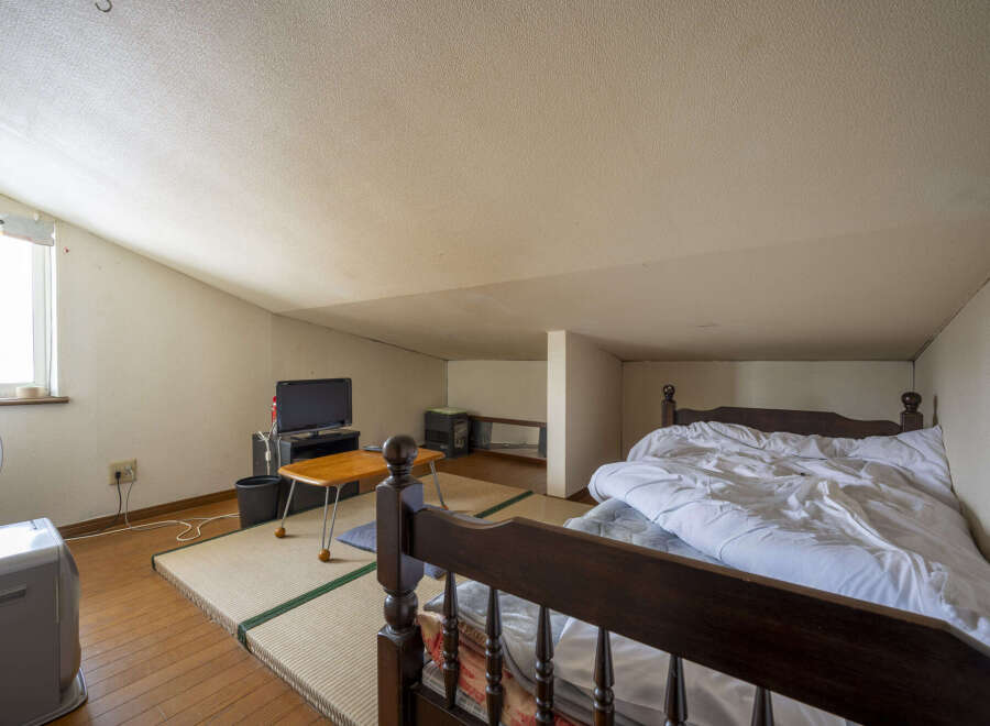 Cozy attic bedroom with tatami mats, a wooden bed frame, and a small TV.