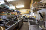This commercial kitchen is fully equipped with stainless steel sinks, countertops, and shelving.