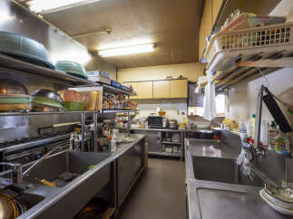 This commercial kitchen is fully equipped with stainless steel sinks, countertops, and shelving.