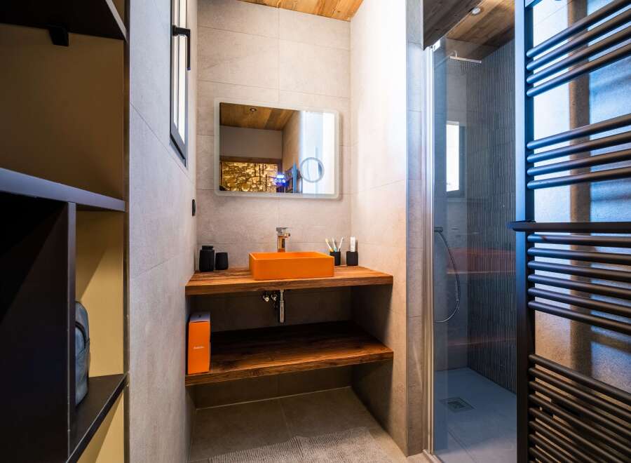 Modern bathroom with stylish orange sink and wooden shelving.